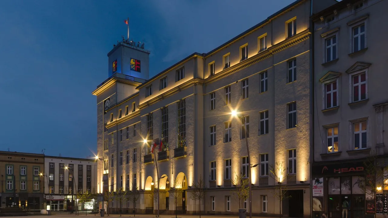 Nocny widok na oświetlony budynek Urzędu Miasta w Chorzowie.